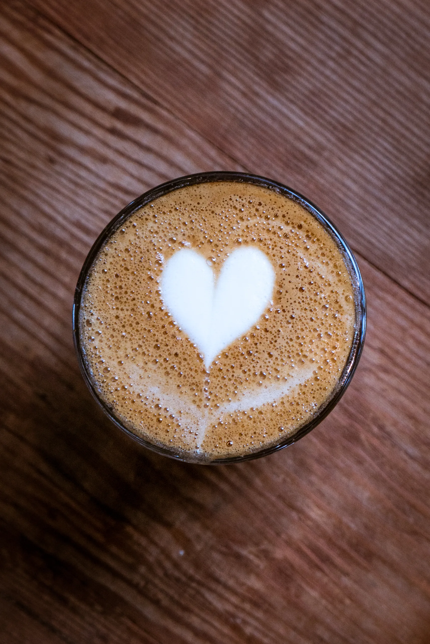 A latte sitting on a wooden table with a milk heart