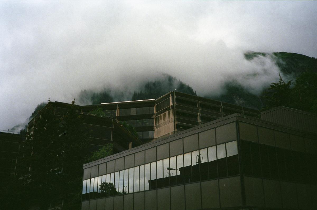 A dramatic photo of a brutalist building with misty mountains in the background