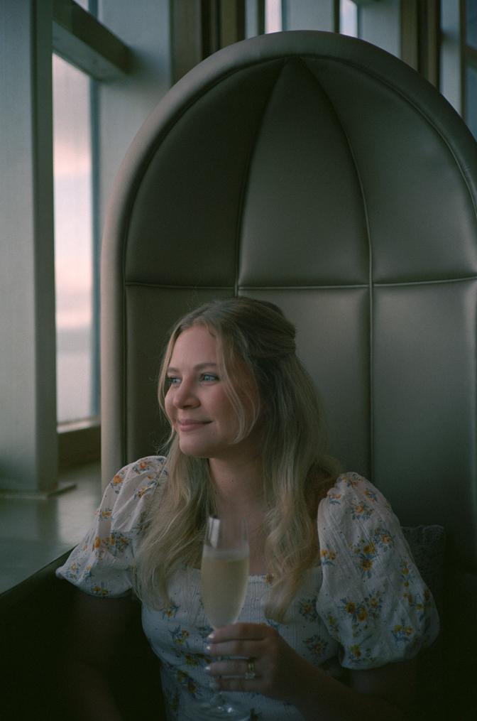 My wife Blake sitting at the dinner table smiling and holding a glass of champagne while looking out of the window