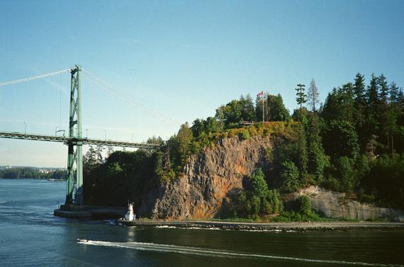 A photo of a boat driving in front of an island with trees and a suspension bridge