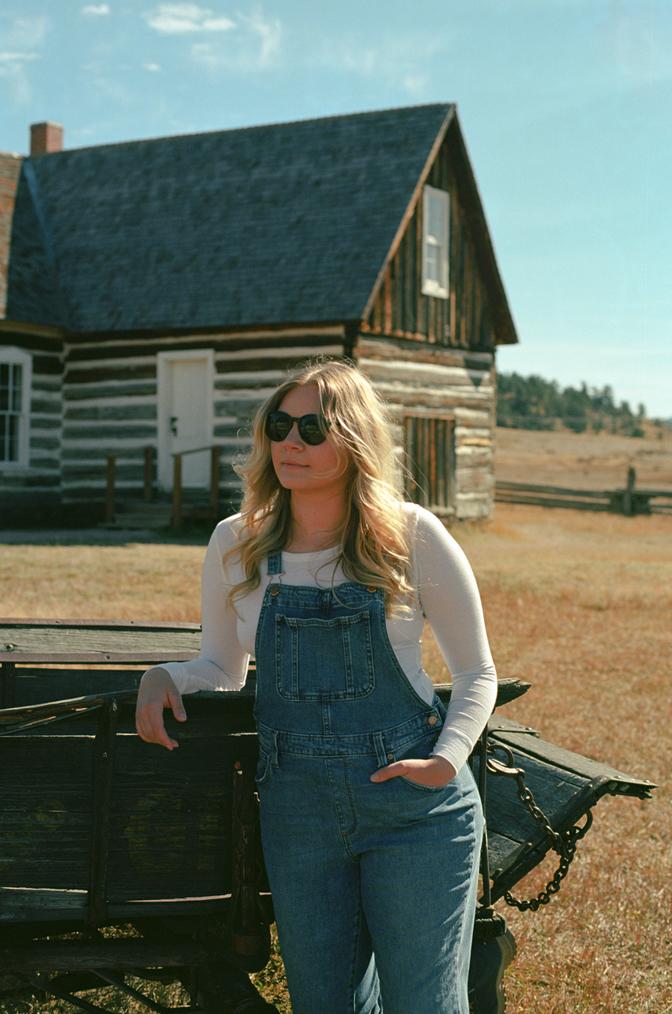 My wife Blake leaning against a horse cart in front of a wooden building