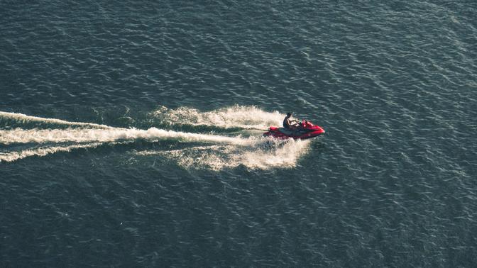 A man riding a red jetski across the water, with a very long wake