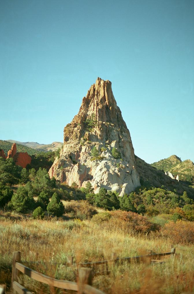 A tall, white rock surrounded by grassy hills in front of a teal sky