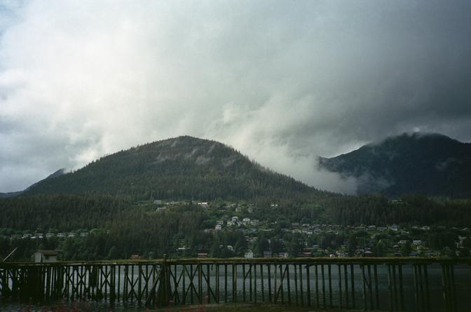 A long wooden pier in front of the city of Juneau, just below a foggy mountain